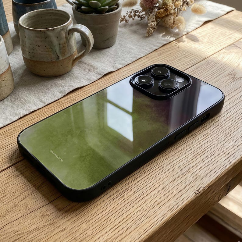 May include: A black phone case with a green and purple gradient design. The case has a glossy finish and a black border. The camera lenses are visible at the top. The case is on a wooden surface.