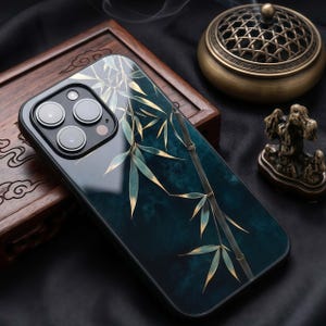 May include: A black smartphone case with a bamboo design. The case features a dark teal background with gold and green bamboo stalks and leaves. The phone case has a black border and a camera cutout.