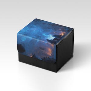 Puede incluir: Una caja negra texturizada con una tapa que presenta un diseño de paisaje de fantasía azul y naranja. La caja tiene forma cuadrada y una superficie texturizada, adecuada para guardar objetos pequeños.