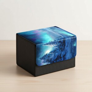 May include: A black storage box with a textured surface and a lid featuring a vibrant blue and purple landscape design. The artwork depicts a mountain range under a bright, glowing sky.