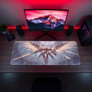 May include: A large rectangular gaming mouse pad featuring a detailed illustration of a white and gold mechanical figure with outstretched wings. The pad is on a dark wooden desk, with a computer monitor and speakers in the background.