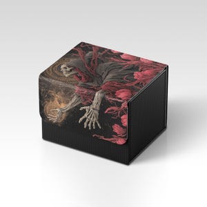 May include: Black card storage box with a detailed illustration of a skeletal figure in a dark cloak reaching out. The artwork features red accents and a golden orb, set against a dark background. The box has a textured finish.