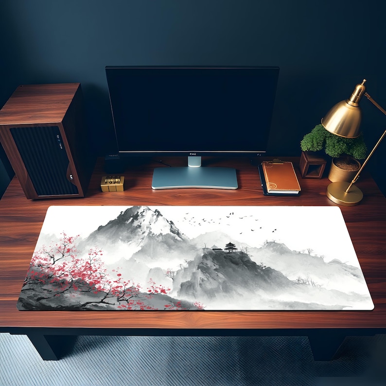Puede incluir: Alfombrilla de rat&oacute;n rectangular con un paisaje asi&aacute;tico sereno. El dise&ntilde;o muestra monta&ntilde;as brumosas, una pagoda y flores de cerezo en tonos grises, negros y rojos. La alfombrilla est&aacute; sobre un escritorio de madera con un monitor.