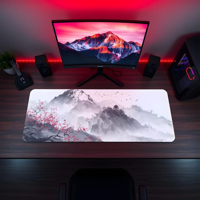 Puede incluir: Alfombrilla de rat&oacute;n rectangular con un sereno paisaje de monta&ntilde;a y flores de cerezo. El dise&ntilde;o es en tonos grises y blancos, con toques de rosa. La alfombrilla est&aacute; sobre un escritorio de madera oscura, con un monitor de ordenador y altavoces en el fondo.