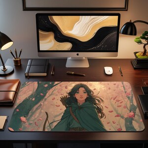Puede incluir: Alfombrilla de escritorio rectangular con una ilustración de estilo anime de una arquera en un bosque. La arquera lleva una capa verde y tiene el pelo largo y oscuro. Pétalos de flores rosas flotan. La alfombrilla está sobre un escritorio de madera oscura con ordenador y accesorios.