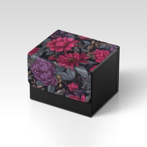 May include: A black box with a floral design on the lid. The flowers are various shades of pink and purple, with green and gray leaves. The box has a textured surface.