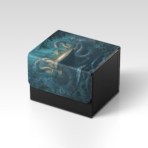 Könnte beinhalten: Eine schwarze, strukturierte Box mit einem Klappdeckel. Der Deckel zeigt eine detaillierte Illustration einer schlangenartigen Kreatur in Blau- und Grüntönen. Die Box dient wahrscheinlich zur Aufbewahrung kleiner Gegenstände.