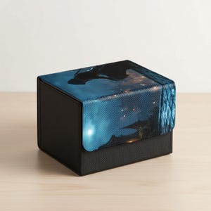 Op de afbeelding: Een zwarte opbergdoos met een getextureerde, koolstofvezelachtige basis en een deksel met een blauw en zwart grafisch ontwerp. Het ontwerp van het deksel toont een nachtscène met een silhouet en gloeiende lichten.