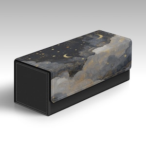 Pode incluir: Uma caixa de armazenamento retangular com base preta texturizada e tampa articulada com um design impresso de céu noturno escuro, nuvens cinzentas, luas crescentes douradas e estrelas douradas dispersas, com costuras visíveis nas bordas.