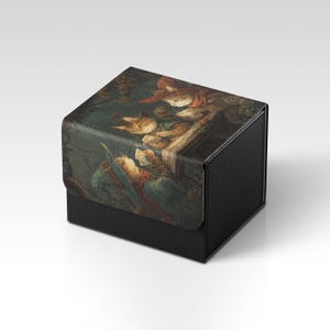 Könnte beinhalten: Eine schwarze, strukturierte Box mit einem Klappdeckel. Der Deckel zeigt ein detailliertes Gemälde von Katzen im Vintage-Stil. Das Kunstwerk ist überwiegend braun, beige und blau. Die Box ist quadratisch und scheint aus einem strapazierfähigen Material zu bestehen.