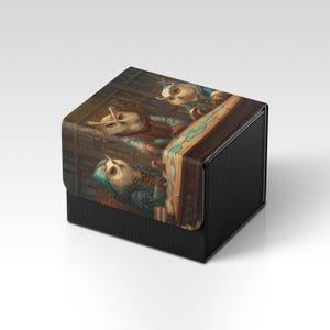 Könnte beinhalten: Eine schwarze, strukturierte Box mit einem Klappdeckel. Der Deckel zeigt eine detaillierte Illustration im Vintage-Stil von eulenartigen Figuren in aufwendiger Kleidung. Die Box dient wahrscheinlich zur Aufbewahrung oder Präsentation.