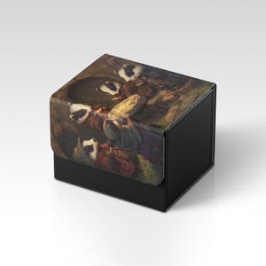 Könnte beinhalten: Eine schwarze Box mit strukturierter Oberfläche. Der Deckel zeigt ein detailliertes Gemälde von Dachsen in einem Wald, mit Braun-, Grün- und Weißtönen. Die Box ist quadratisch und scheint aus einem robusten Material zu bestehen.