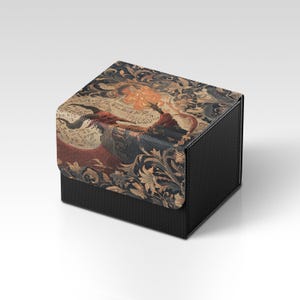 May include: A black box with a textured surface. The lid features a detailed tapestry design with a dragon, floral elements, and text in shades of red, blue, and gold. The box is likely for storage or display.