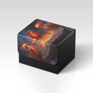 Könnte beinhalten: Eine schwarze, strukturierte Box mit Deckel, die eine lebendige Illustration von Phönixen in Orange- und Rottönen vor einem dunkelblauen und orangefarbenen Hintergrund zeigt. Die Box dient wahrscheinlich zur Aufbewahrung von Karten oder kleinen Gegenständen.
