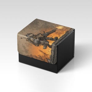 Puede incluir: Una caja negra con superficie texturizada y tapa con bisagras. La tapa presenta una ilustración detallada de un soldado futurista con un arma grande, sobre un fondo anaranjado y ardiente. La caja es probablemente para almacenamiento.