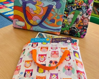 May include: Three rectangular fabric book bags with handles. One bag features a colorful landscape with a sun and palm tree, another has a dark background with various cartoon monster faces, and the third is white with a repeating pattern of colorful owls.