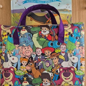Pu&ograve; includere: Una borsa tote rettangolare in tessuto con una stampa colorata all-over di vari personaggi animati del franchise Toy Story, tra cui Woody, Buzz Lightyear e Lotso. La borsa ha due manici in tessuto viola fissati sul bordo superiore.
