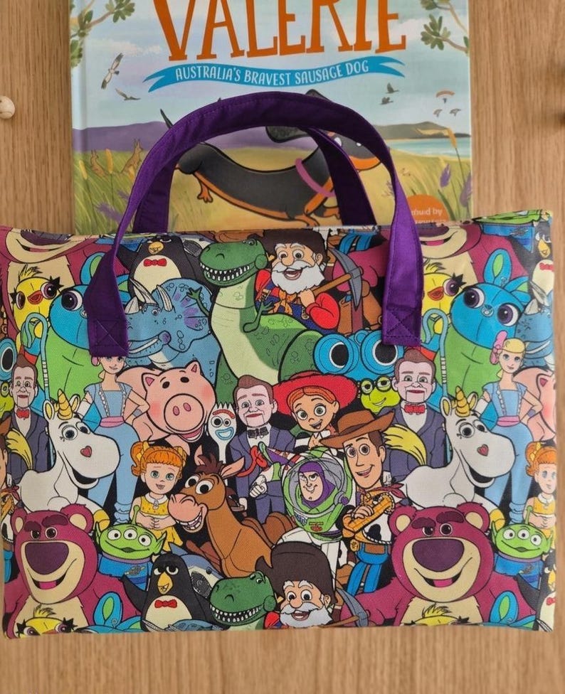 Pu&ograve; includere: Una borsa tote rettangolare in tessuto con una stampa colorata all-over di vari personaggi animati del franchise Toy Story, tra cui Woody, Buzz Lightyear e Lotso. La borsa ha due manici in tessuto viola fissati sul bordo superiore.