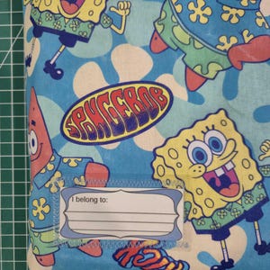 Pu&ograve; includere: Una custodia in tessuto con un motivo ripetuto di SpongeBob SquarePants e Patrick Stella su uno sfondo azzurro con forme di fiori bianchi. Un'etichetta rettangolare bianca con il testo I belong to: &egrave; cucita sulla parte anteriore.