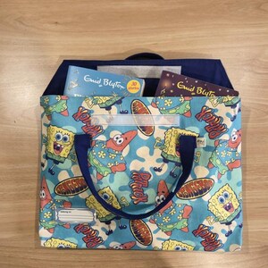 Pu&ograve; includere: Una borsa in tessuto blu per libri con un motivo ripetuto dei personaggi SpongeBob SquarePants e Patrick Stella. La borsa presenta manici blu scuro, una chiusura a strappo e un'etichetta bianca con la scritta "Belong to" stampata sul davanti.