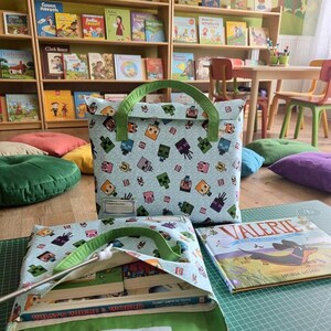 Pu&ograve; includere: Due borse in tessuto azzurro con un motivo ripetuto di personaggi pixelati. Le borse hanno manici in tessuto verde e una chiusura in velcro bianca. Una borsa &egrave; in posizione verticale, mentre l'altra &egrave; aperta e mostra dei libri all'interno.