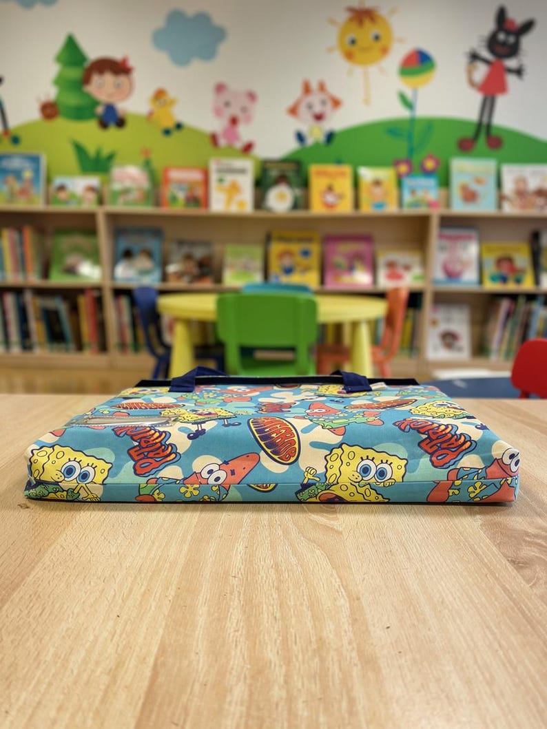 Pu&ograve; includere: Un oggetto rettangolare, piatto e rivestito in tessuto con una vivace stampa all-over di SpongeBob SquarePants e Patrick Stella su sfondo azzurro. L'oggetto presenta manici in tessuto blu scuro e una tasca in plastica trasparente per etichette.