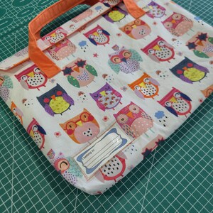 May include: A white fabric document case featuring a repeating pattern of colorful owls in shades of pink, orange, purple, and blue. The case has orange fabric handles and a rectangular label on the front with the printed text "I belong to:".