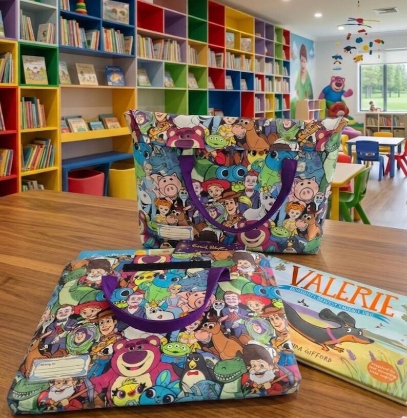 Pu&ograve; includere: Due borse in tessuto con una stampa colorata di vari personaggi di film d'animazione, tra cui un orso rosa, un cowboy e un ranger spaziale. Ogni borsa ha manici viola e una piccola etichetta rettangolare bianca per scrivere un nome.