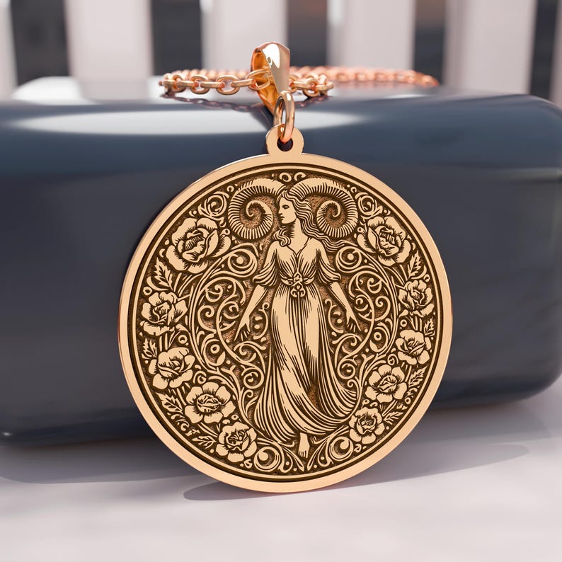 May include: A gold-colored pendant necklace featuring a detailed circular design. The pendant showcases a woman figure surrounded by roses and ornate scrollwork. The necklace has a delicate chain and a decorative bail.
