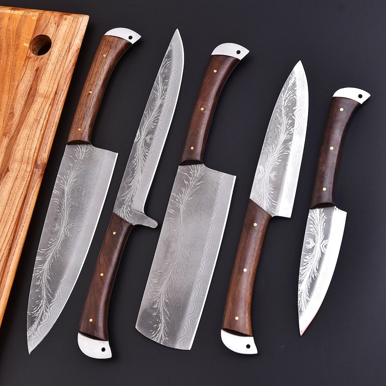 May include: Set of five kitchen knives with dark wood handles and silver blades. The blades feature a decorative etched pattern. The handles are secured with brass rivets and have a white accent at the base. A wooden cutting board is visible in the background.