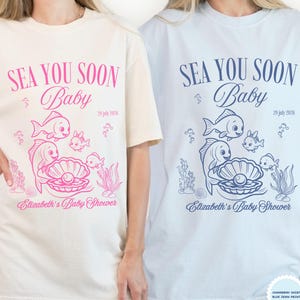 Può includere: Due magliette, una avorio e una azzurra, con la scritta "SEA YOU SOON Baby" e un motivo a tema marino. Il motivo include pesci, una perla in un'ostrica e la scritta "Elizabeth's Baby Shower".