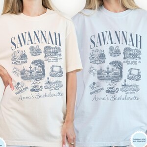 Pu&ograve; includere: Due magliette, una color avorio e una azzurra, con un design grafico che include la parola "Savannah" e illustrazioni di monumenti locali. &Egrave; incluso anche il testo "Anna's Bachelorette".