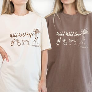 May include: An ivory t-shirt with brown text reading Wild, Wild Wife and an espresso t-shirt with ivory text reading Wild, Wild Crew. Both shirts feature line art graphics of a champagne bottle, a diamond ring, martini glasses, and a disco ball.