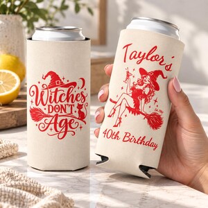 May include: Two beige slim can coolers with red graphics. One features a witch hat, broom, cat, and the text Witches Don't Age. The other shows a witch on a broom holding a drink with the text Taylor's 40th Birthday and Est. 1987.