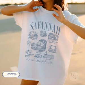 Pu&ograve; includere: T-shirt bianco con stampa blu jeans con la scritta "SAVANNAH" e varie illustrazioni di monumenti di Savannah. La maglietta include anche il testo "Anna's Bachelorette".