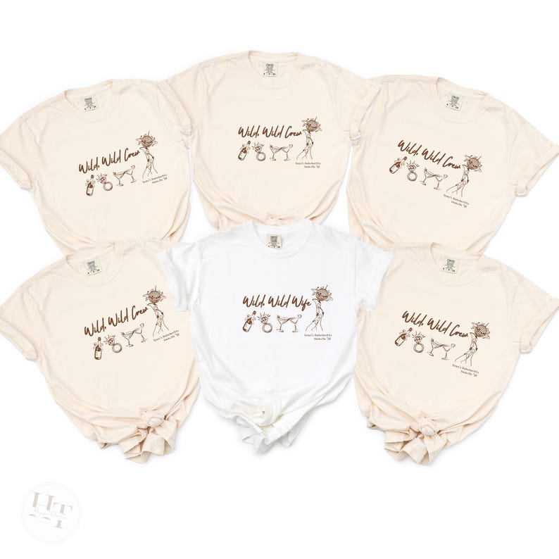 May include: Five cream-colored t-shirts and one white t-shirt featuring a brown line-art graphic. The design includes the text 'Wild Wild Crew' or 'Wild Wild Wife' alongside illustrations of a champagne bottle, a ring, a cocktail glass, and a sunflower.