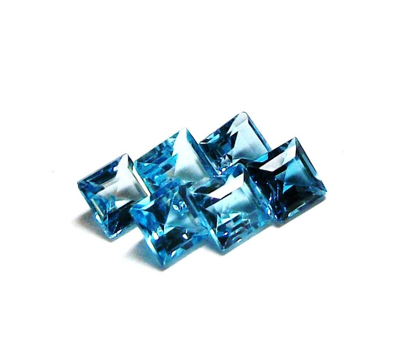 May include: Six square-shaped, faceted, blue topaz gemstones. The gemstones are arranged in a staggered pattern.