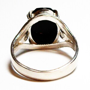 Puede incluir: Un anillo de plata con una piedra ovalada negra engastada en un dise&ntilde;o simple y elegante.