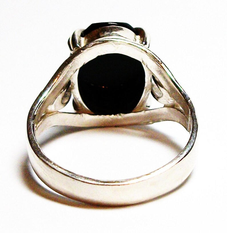 Puede incluir: Un anillo de plata con una piedra ovalada negra engastada en un dise&ntilde;o simple y elegante.