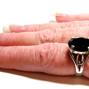 Puede incluir: Un anillo de plata con una gran piedra preciosa negra de forma ovalada. El anillo est&aacute; engastado en un dise&ntilde;o simple y elegante.