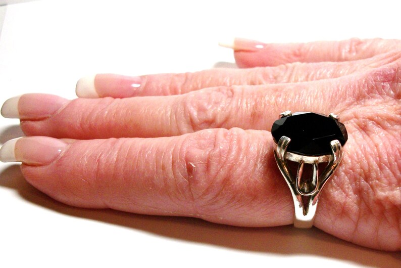 Puede incluir: Un anillo de plata con una gran piedra preciosa negra de forma ovalada. El anillo est&aacute; engastado en un dise&ntilde;o simple y elegante.