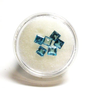 May include: A small plastic container filled with loose, faceted, blue topaz gemstones.