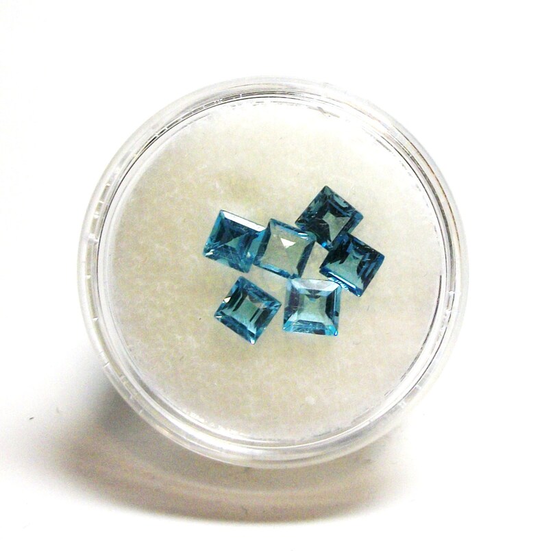 May include: A small plastic container filled with loose, faceted, blue topaz gemstones.