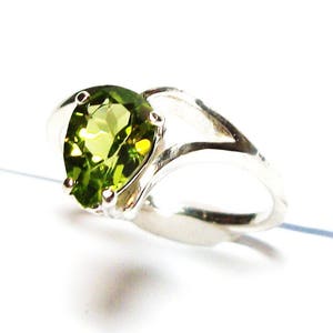 May include: A silver ring featuring a heart-shaped green gemstone. The ring has a distinctive twisted band design.