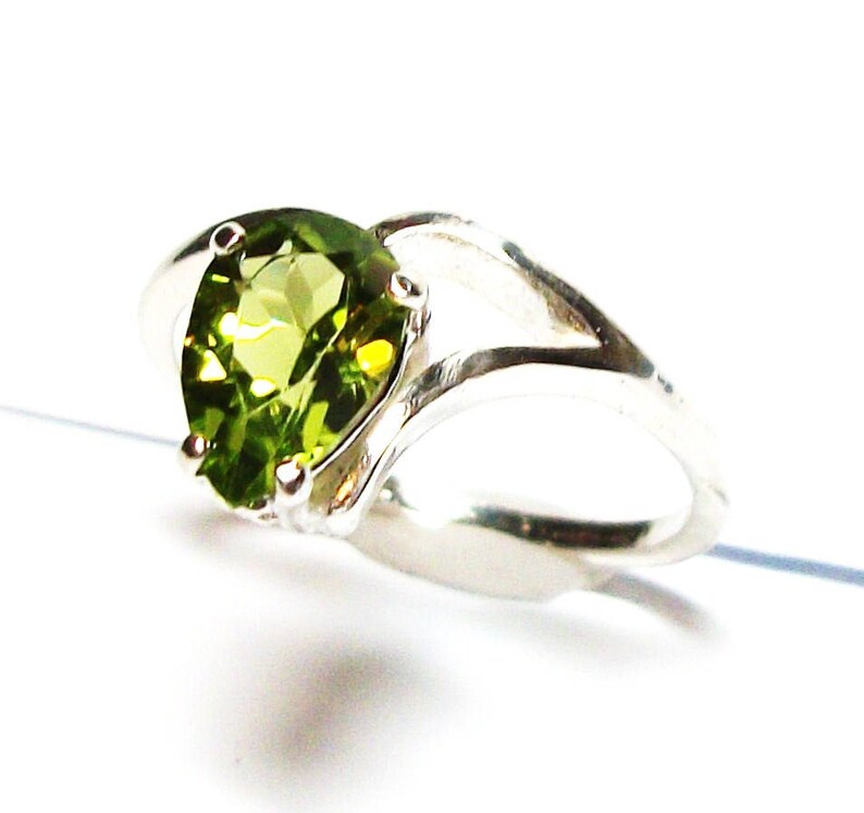May include: A silver ring featuring a heart-shaped green gemstone. The ring has a distinctive twisted band design.