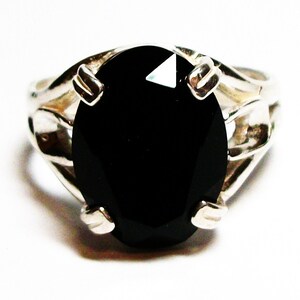 Puede incluir: Un anillo de plata con una gran piedra ovalada negra. El anillo tiene un dise&ntilde;o delicado e intrincado.