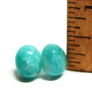 May include: Two round, teal green amazonite gemstone beads, each approximately 1/2 inch in diameter, next to a wooden ruler.