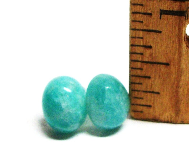 May include: Two round, teal green amazonite gemstone beads, each approximately 1/2 inch in diameter, next to a wooden ruler.