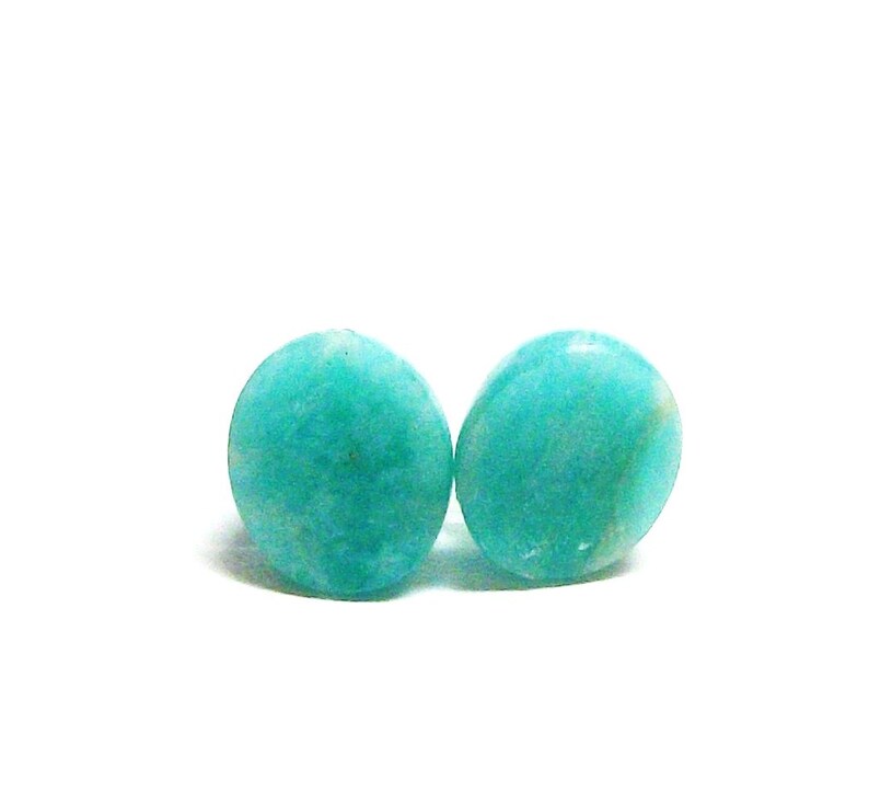 May include: Two round, teal green gemstone earrings. The earrings are smooth and have a slightly mottled appearance.