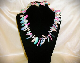 May include: A colorful necklace and bracelet set displayed on a black mannequin. The jewelry features iridescent, shell-like pieces in shades of pink, blue, and green. The necklace is strung with a delicate cord.